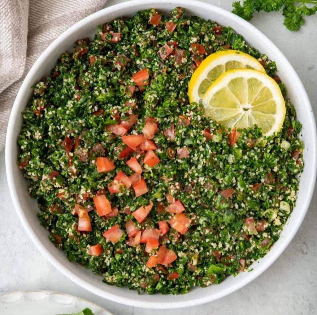 A bowl of vibrant Lebanese tabbouleh with finely chopped parsley, tomatoes, mint, and soaked bulgur, garnished with fresh lemon wedges — a fresh and healthy no‑cook salad.