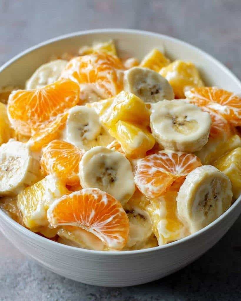 Fresh Banana Orange Creamy Fruit Salad in a bowl with pineapple chunks, Greek yogurt, and honey, ready to serve as a healthy and refreshing snack or dessert
